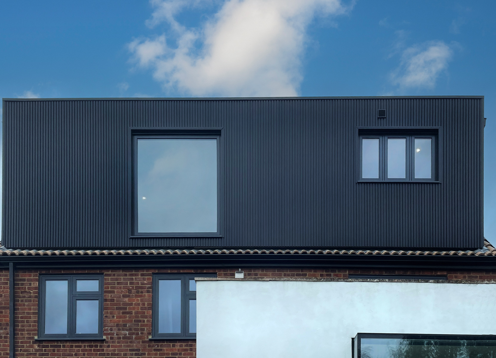 Spacious dormer loft conversion in Buckinghamshire area with black cladding and modern, flush architectural windows in anthracite grey.